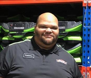 A photo of a smiling male employee wearing a black SERVPRO shirt standing in front of green SERVPRO equipment