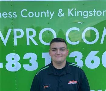 A smiling male employee standing in front of a SERVPRO green truck wearing a black SERVPRO polo shirt