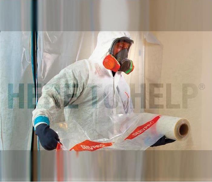 A SERVPRO technician wearing white PPE with a full face mask while unraveling encapsulating plastic material.