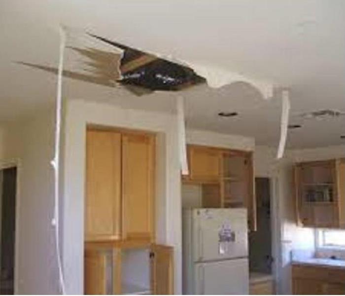 A large hole in the kitchen ceiling showing exposed framing and ripped sheetrock stemming from water damage above it.