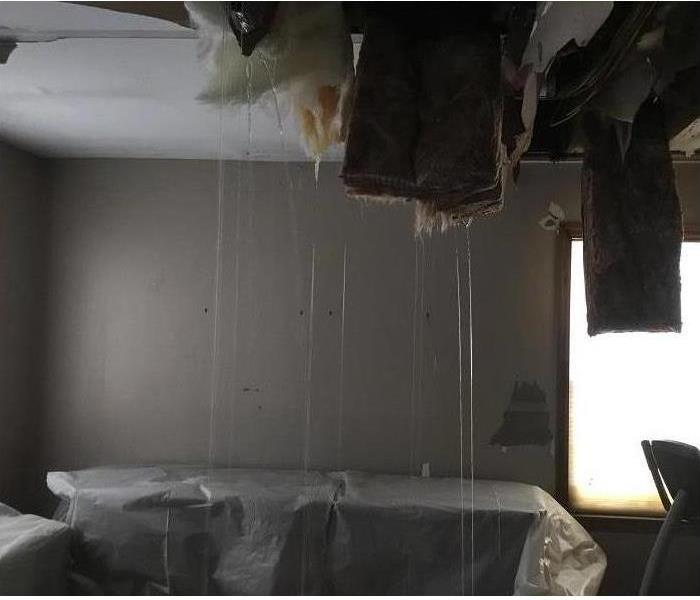 A steady stream of water coming out of a ceiling onto bedroom furniture from a burst pipe in the ceiling.