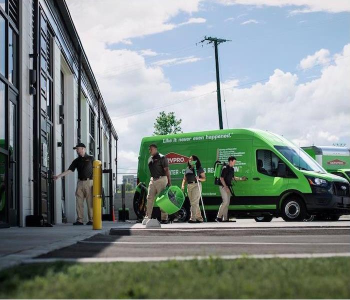 A team of SERVPRO professionals unloading equipment from a green SERVPRO van and bringing it into a commercial building.