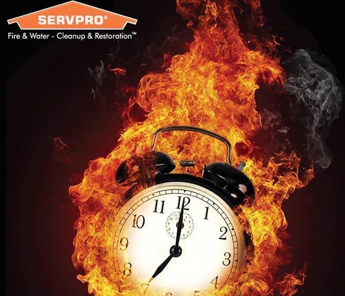 An image of a clock surrounded by flames and the SERVPRO orange house logo showing in the upper left corner of the image.