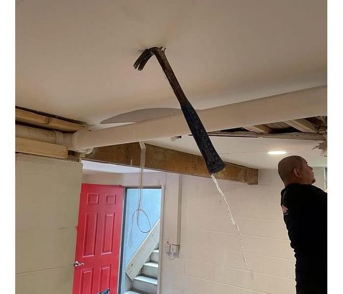 A hammer hanging out of a basement ceiling with water streaming off of it showing an active leak.