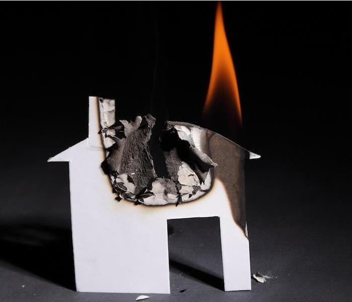 A cardboard cutout of a small white house, on fire on the upper right corner and scorched black on the other parts.